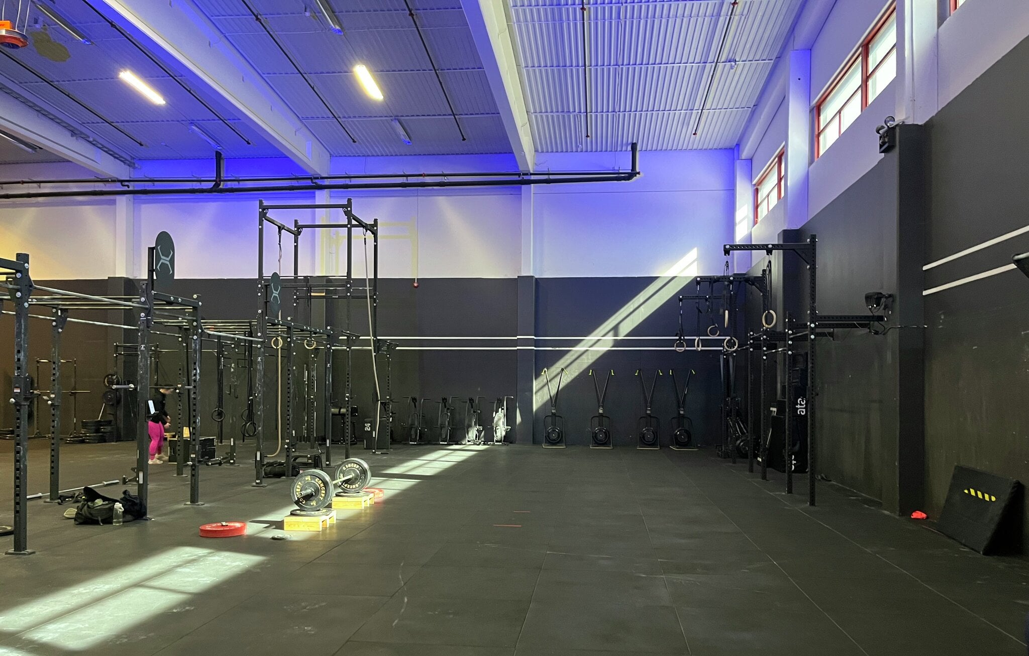 Romslig sal med svarte styrkerigger, turnringer og slyngetrau langs veggene, opplyst av lilla LED-lys. Det store funksjonelle treningsrommet på MOVA Arena Lillehammer har frittstående rigger med pull-up-stenger, turnringer og slyngetrau, samt åpent gulvareal til CrossFit-inspirert trening. Lilla og blått stemningslys gir rommet et moderne preg, og dagslys siver inn fra høye vinduer.
